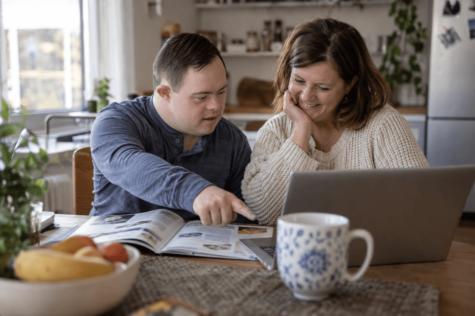 A mother and her adult son, who has Down syndrome, reading a guide together at the kitchen table